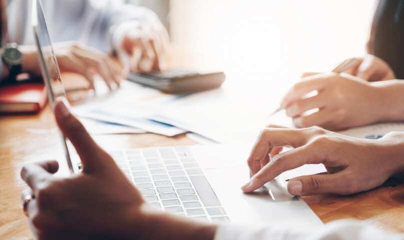 Hände von zwei Personen, Laptop und Unterlagen auf dem Tisch